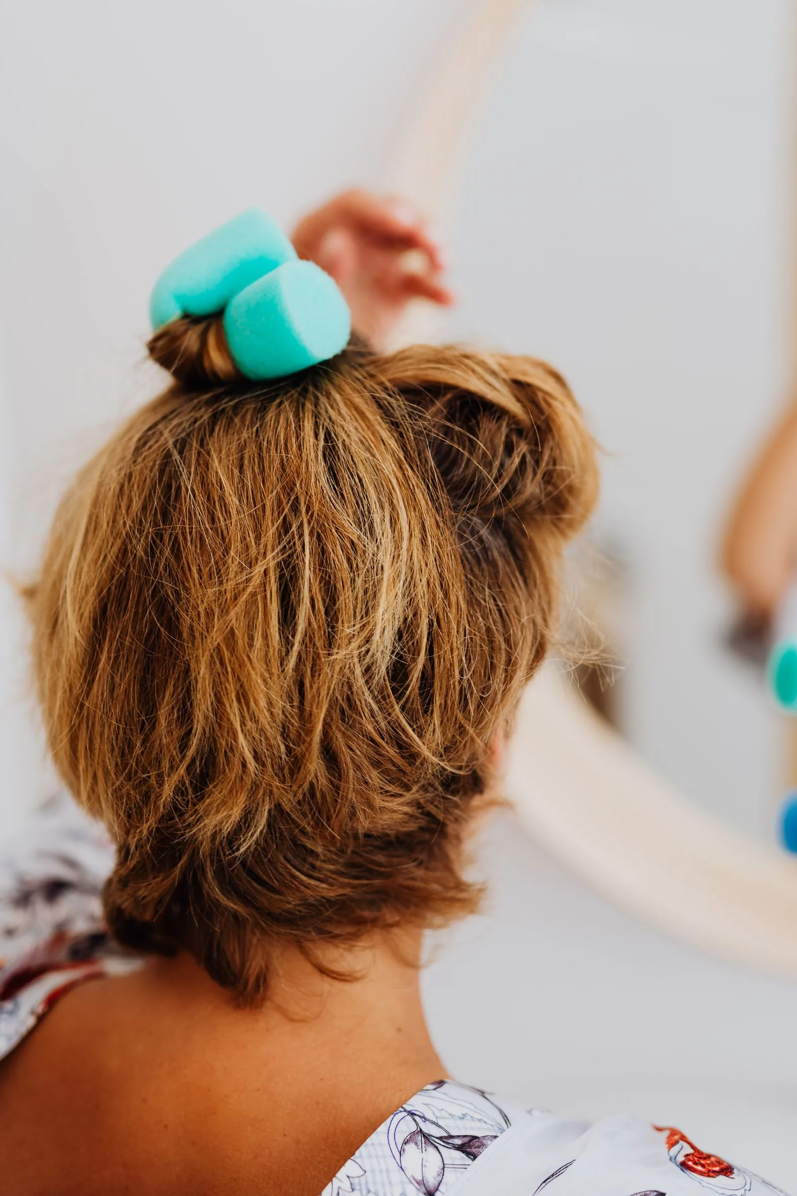 Woman setting her hair in rollers in front of a mirror, styling fine hair for volume