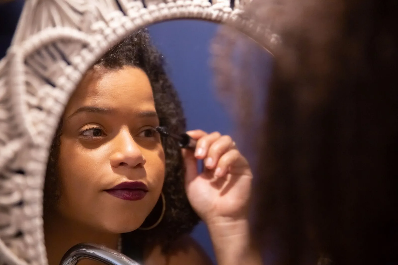 Woman applying mascara in a mirror, illustrating a guide to the best non-clumping mascara